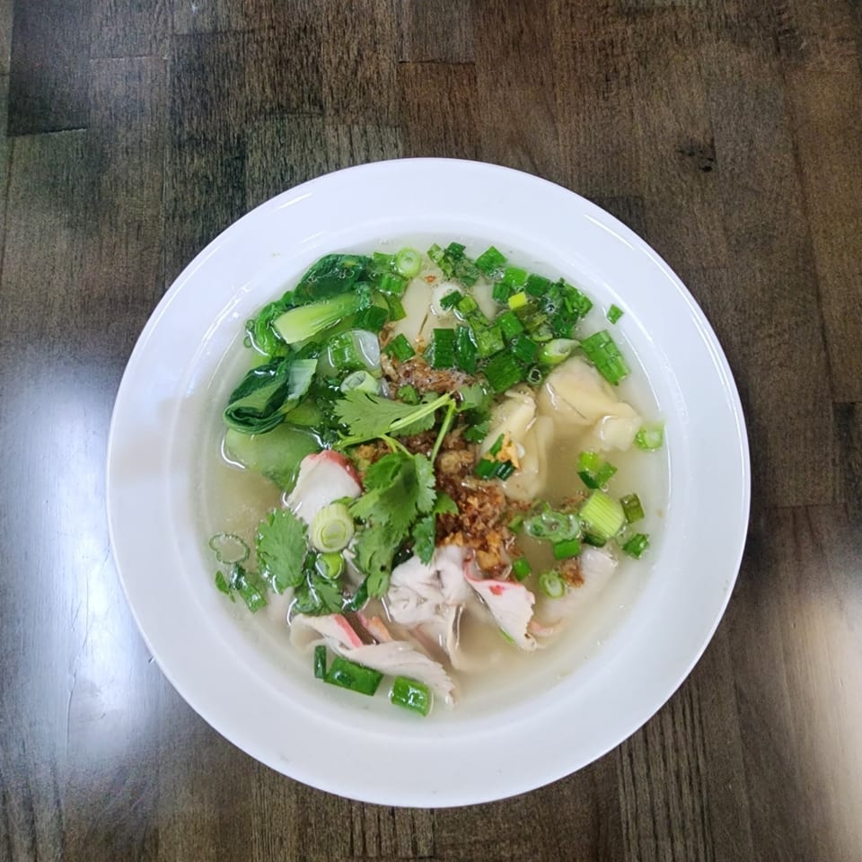 Overhead view of a bowl of Vietnamese wonton soup with pork, bok choy, and green onions.