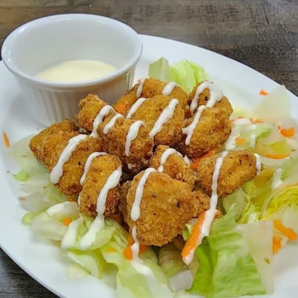 Crispy fried shrimp drizzled with white sauce, served on a bed of lettuce with a side of dipping sauce.
